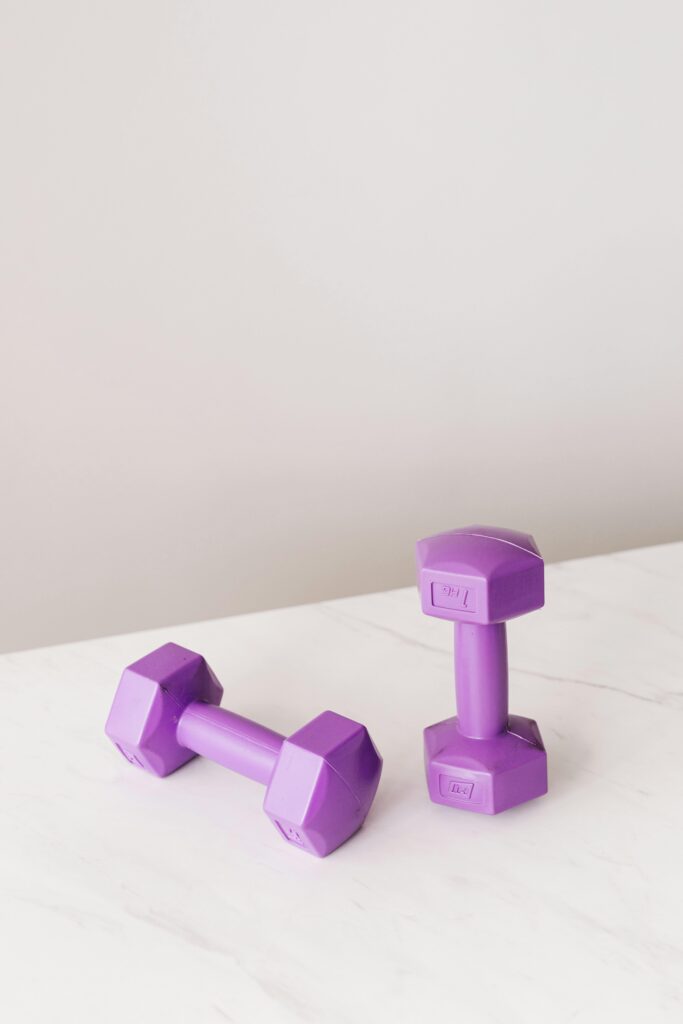 From above of purple dumbbells for fitness training placed on marble surface of table against gray background