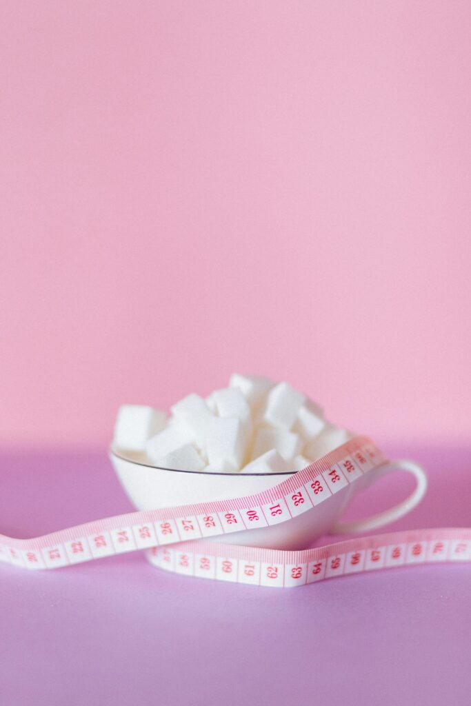 Aesthetic still life of sugar cubes in a bowl with a pink measuring tape on a pastel background.